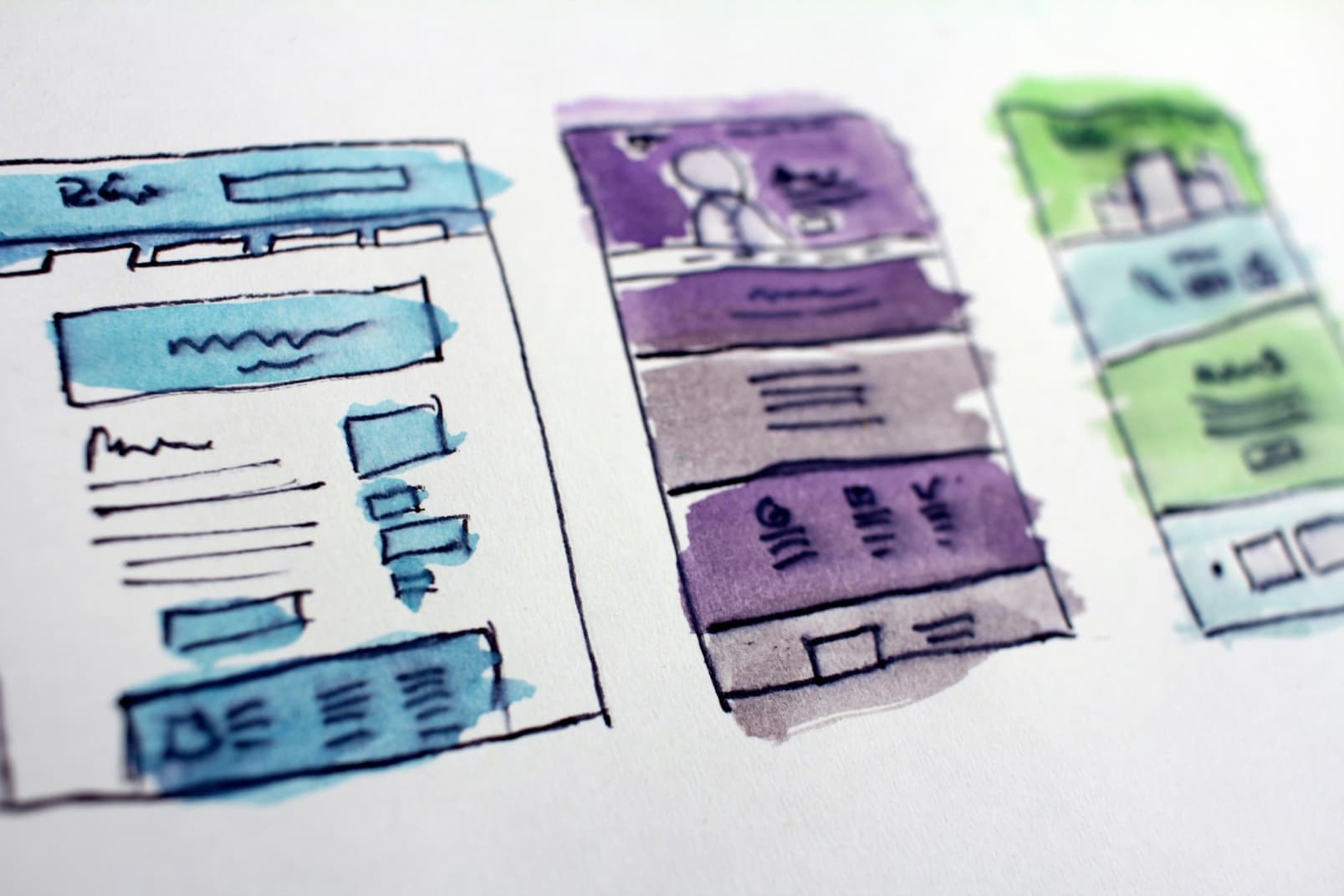 Three separate pages of a User Interface or Web Page design roughly drawn out and filled in with different color schemes by marker or highlighter.